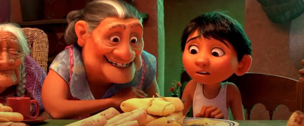 Screenshot from Pixar's Coco with Miguel and Abuela looking at a plate of tamales. She looks excited and he looks nervous.